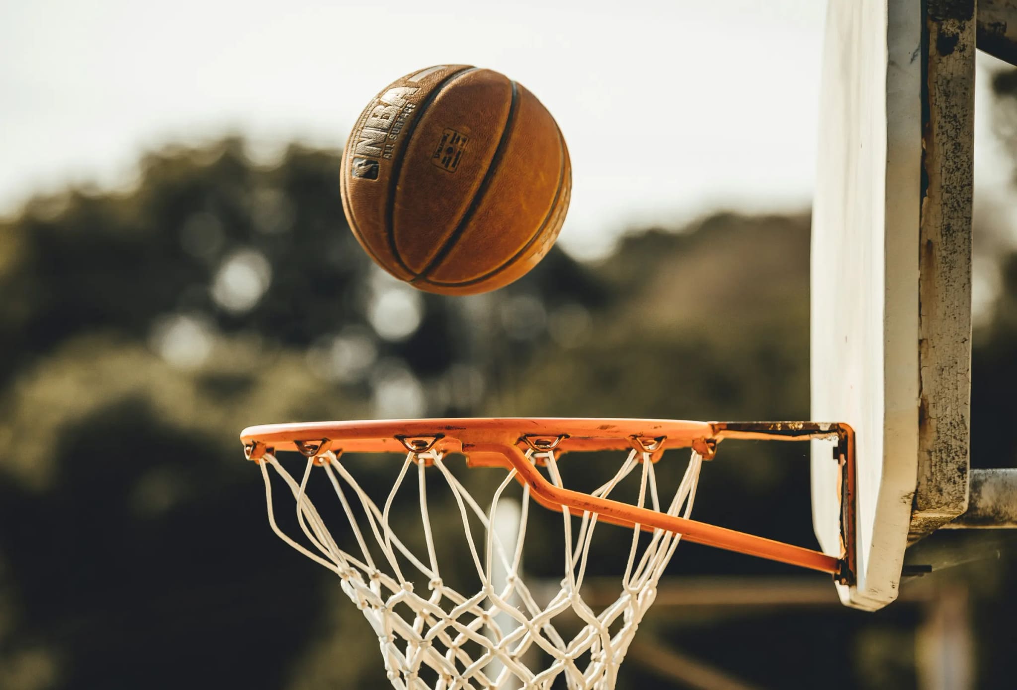 A basketball dropping toward the hoop on an outdoor court, a second hoop blurred behind