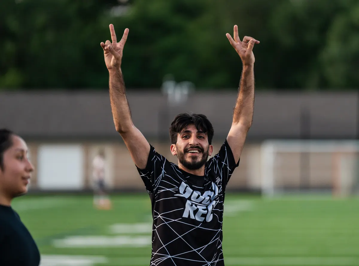 A smiling player in a GoodRec shirt with both arms raised on a turf field