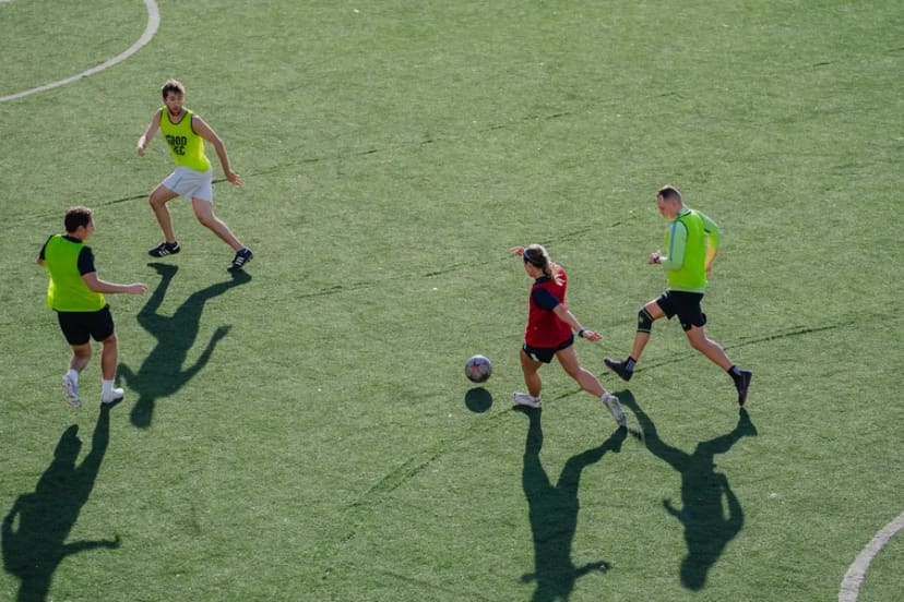Players and their long shadows chasing a ball across turf, seen from above