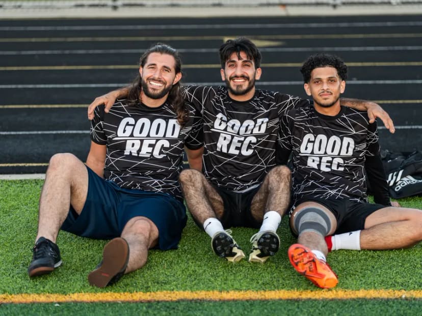 Three players in GoodRec shirts sitting on the turf together after a game