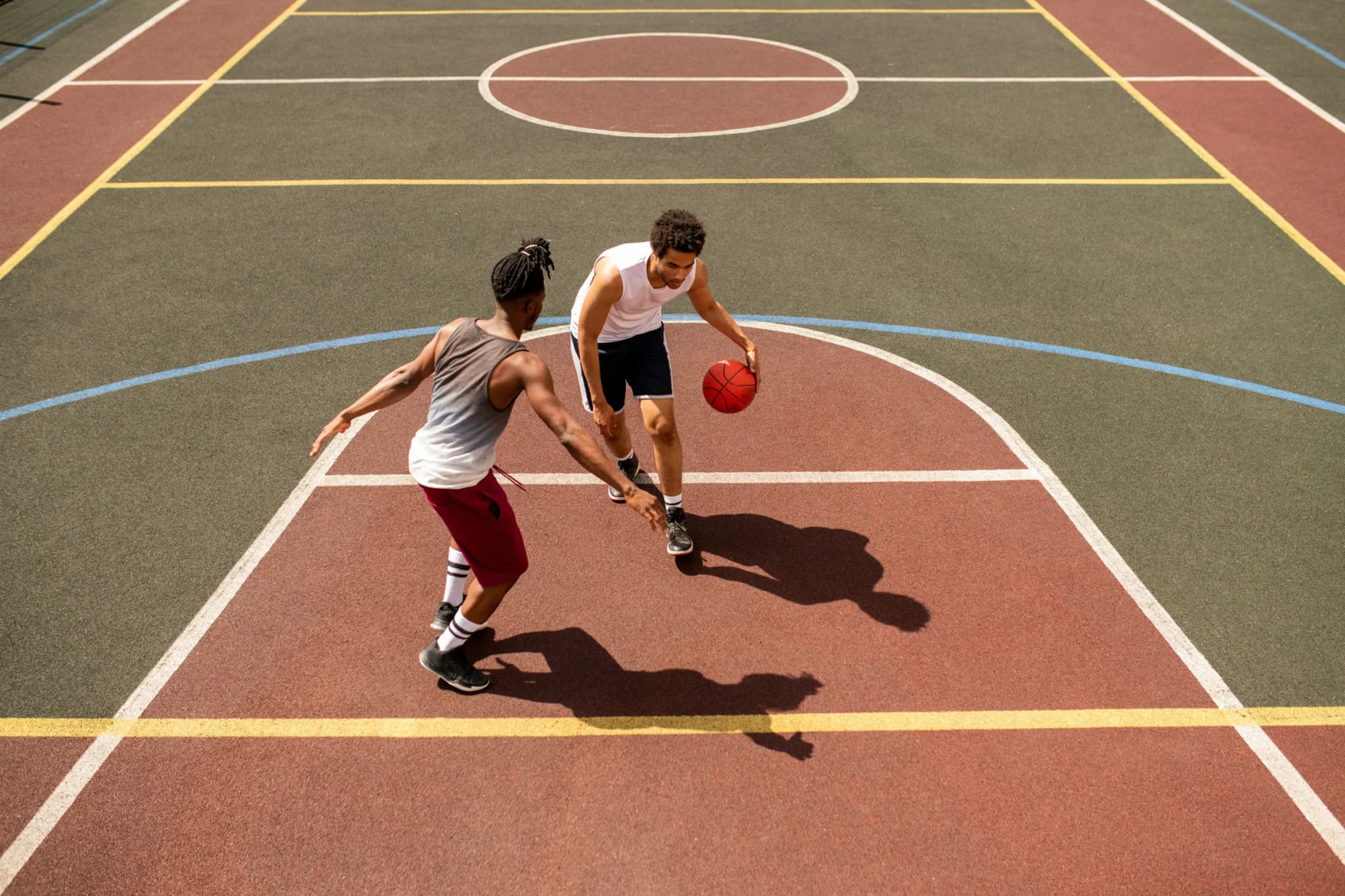Two players going one on one on an outdoor court seen from above, one dribbling into the key as the other reaches in