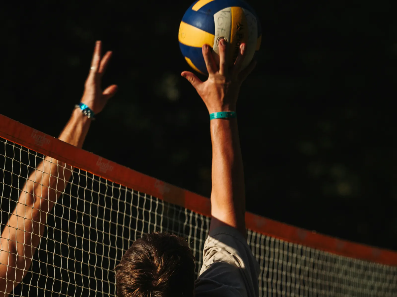 A player reaching above the net to tip the ball over, an opponent’s hand up to block