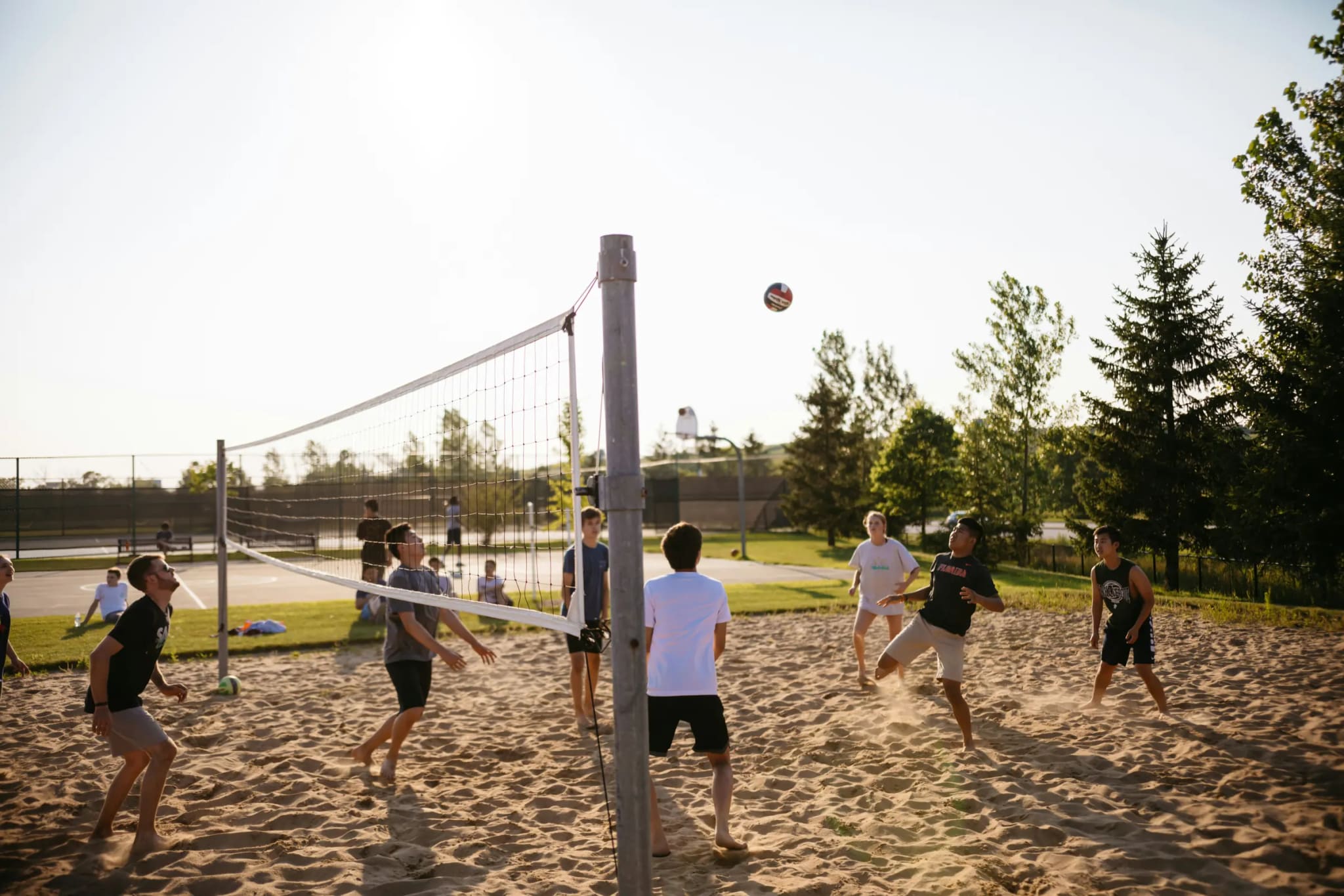 A sand volleyball game in the evening sun, players either side of the net watching the ball drop