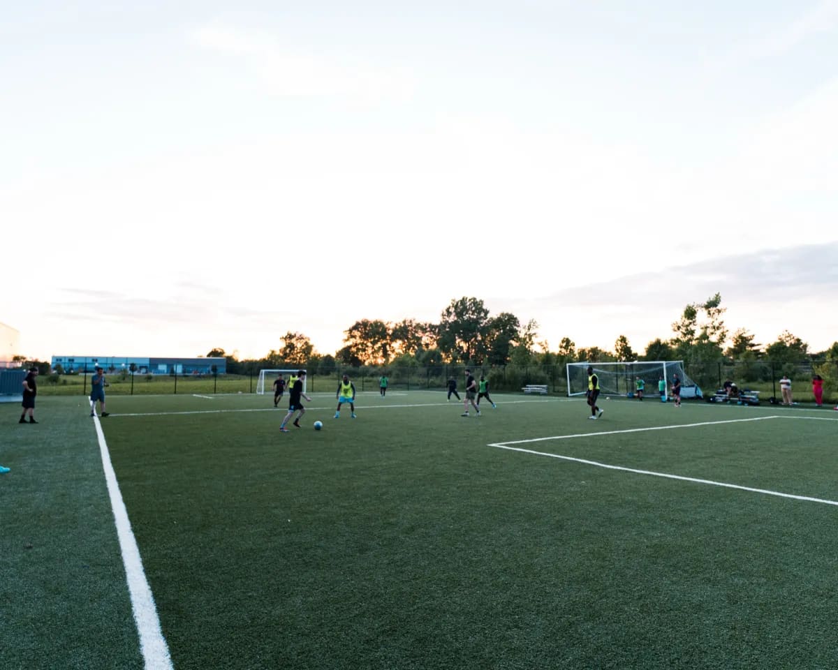 A turf field at dusk with a pickup game underway in the distance