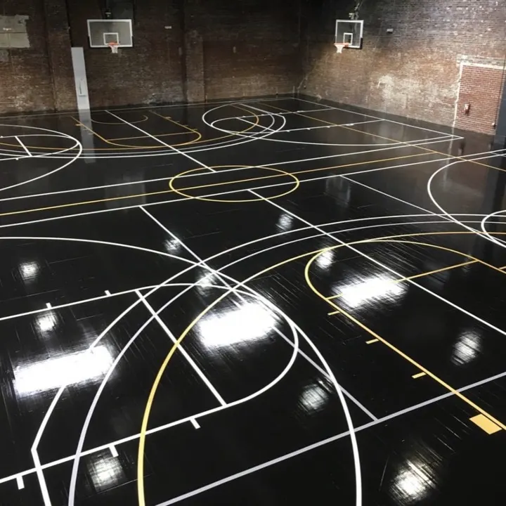 An empty indoor gym with a glossy black court marked in white and gold lines, hoops on the brick walls