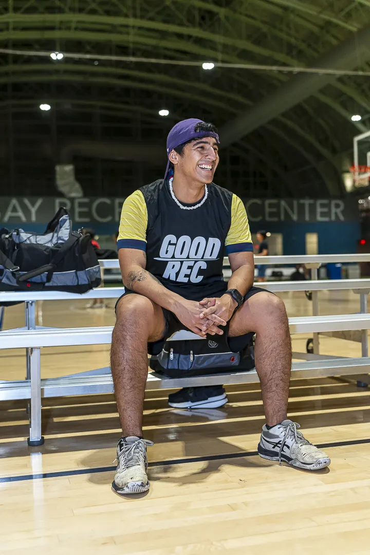 A player in a GoodRec bib sitting on the bleachers of an indoor court, waiting for the game
