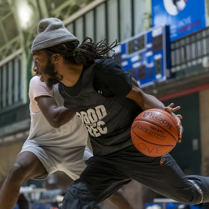 A player in a GoodRec bib driving with the ball past a defender on an indoor court