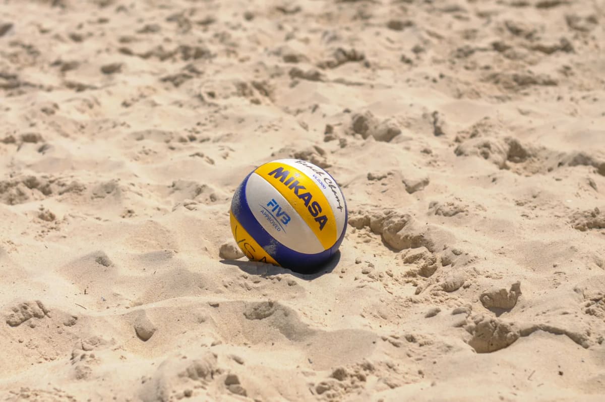 A volleyball resting on the sand of an outdoor court