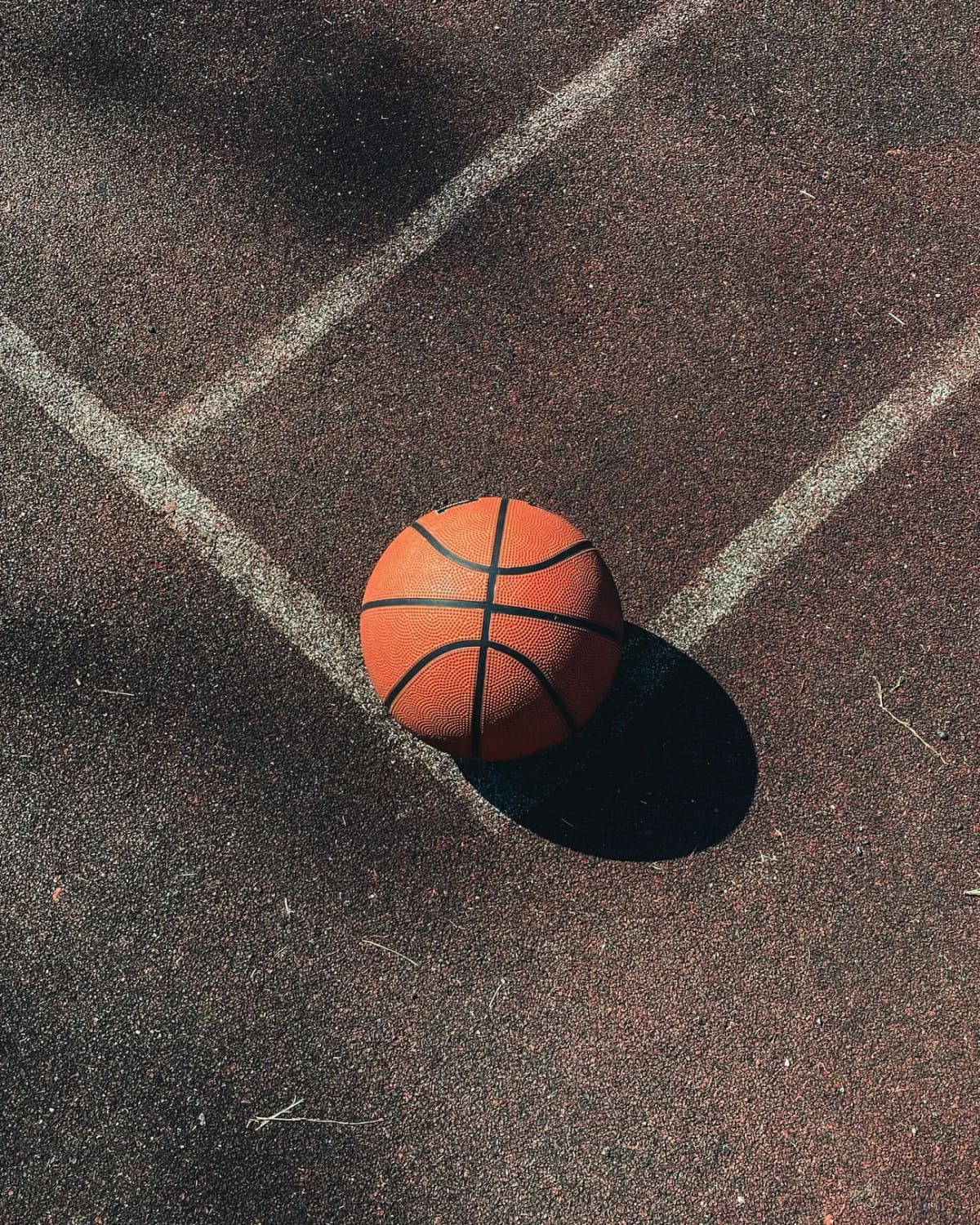 A basketball resting on the line of an outdoor court