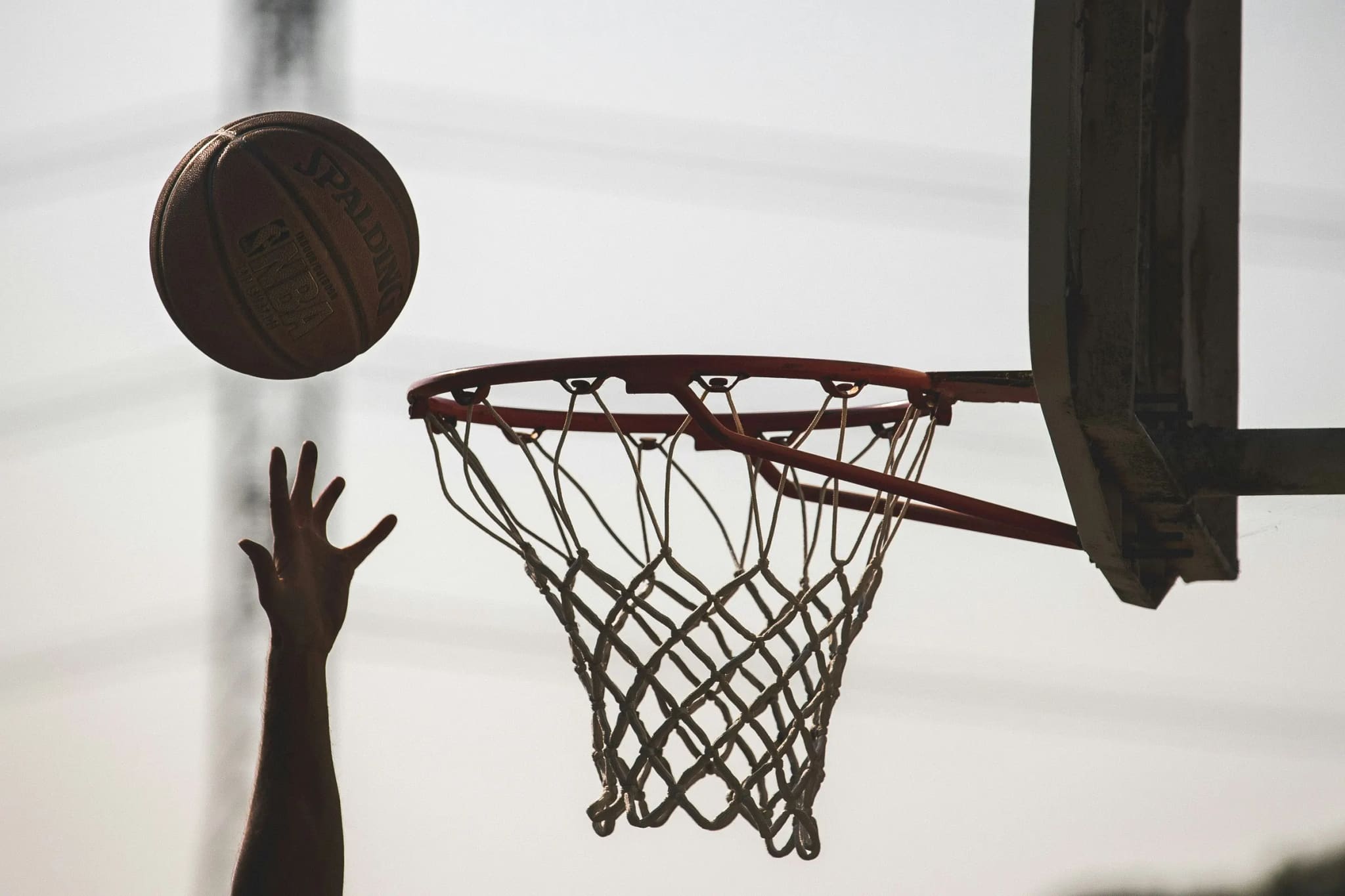 A hand reaching up as the ball drops towards the hoop on an outdoor court at dusk