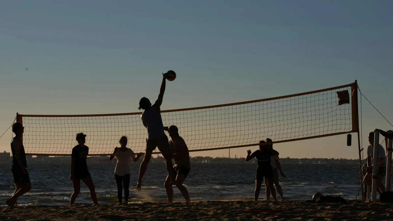 A beach volleyball game at sunset, one player jumping at the net to spike the ball
