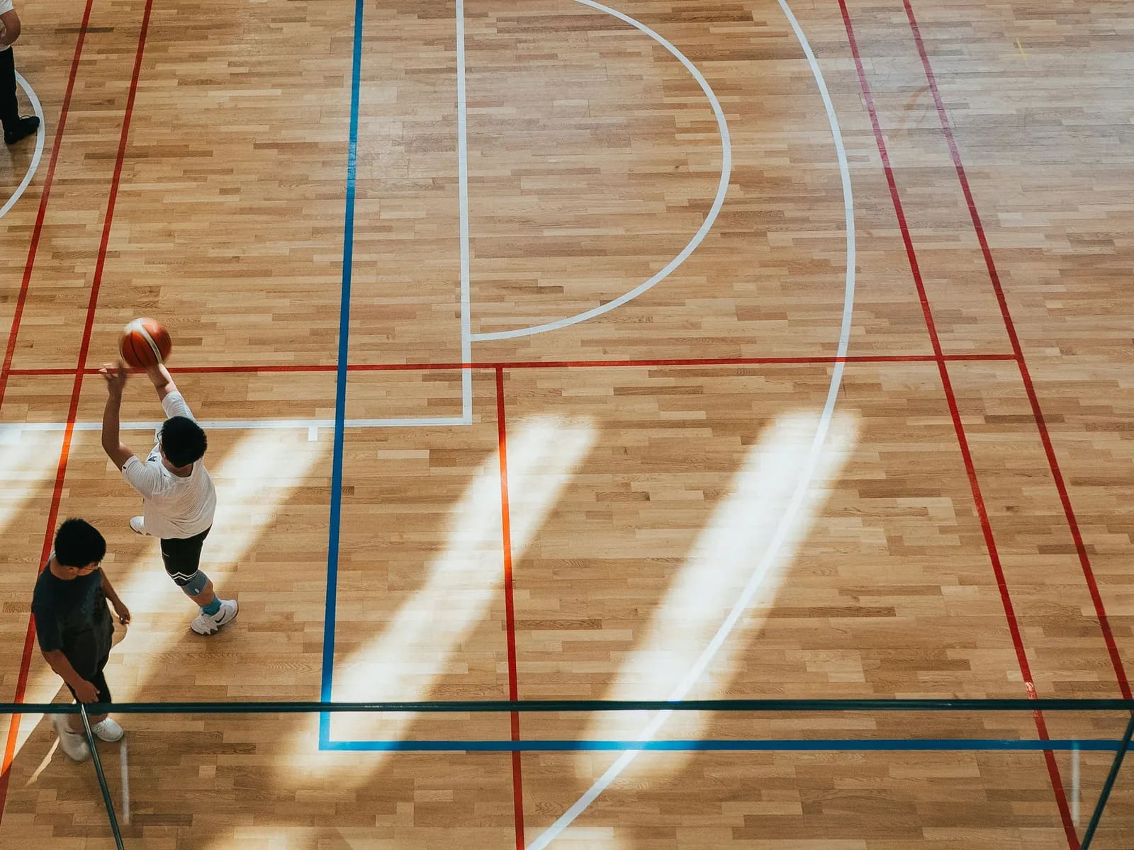 An indoor court seen from above, a player rising for a shot at the edge of it