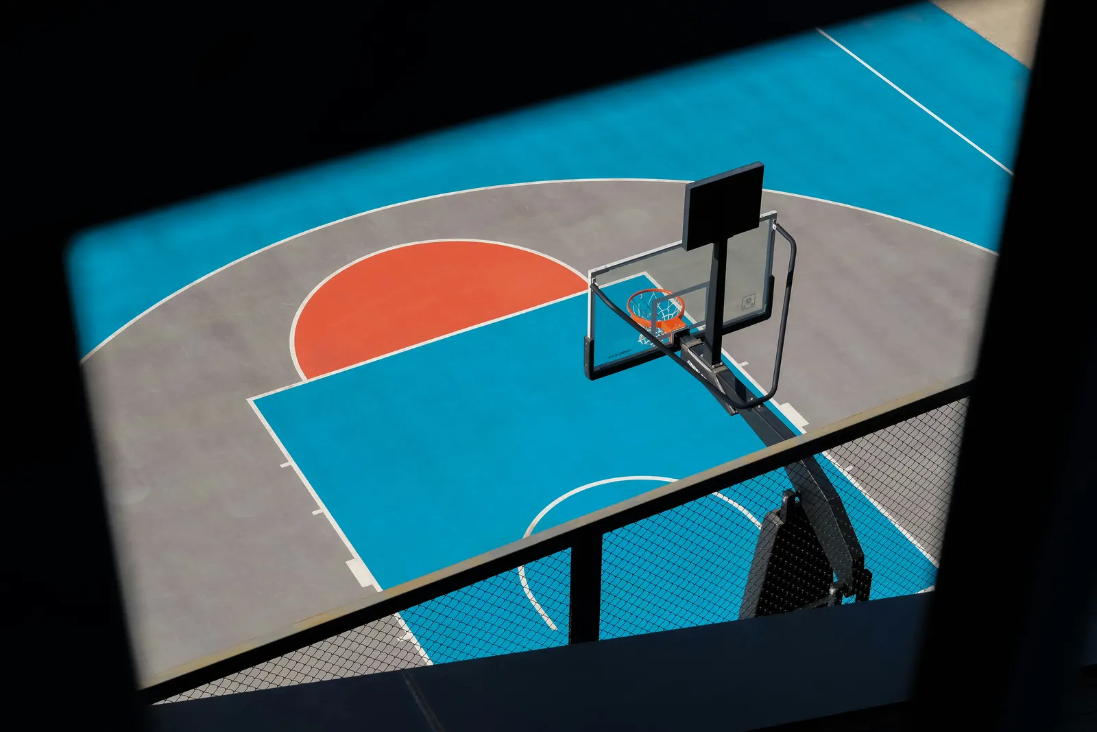 An empty outdoor court seen from above, its hoop standing over a blue and orange key