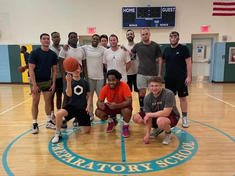 A group of players posing on the center circle of an indoor gym after a GoodRec basketball game