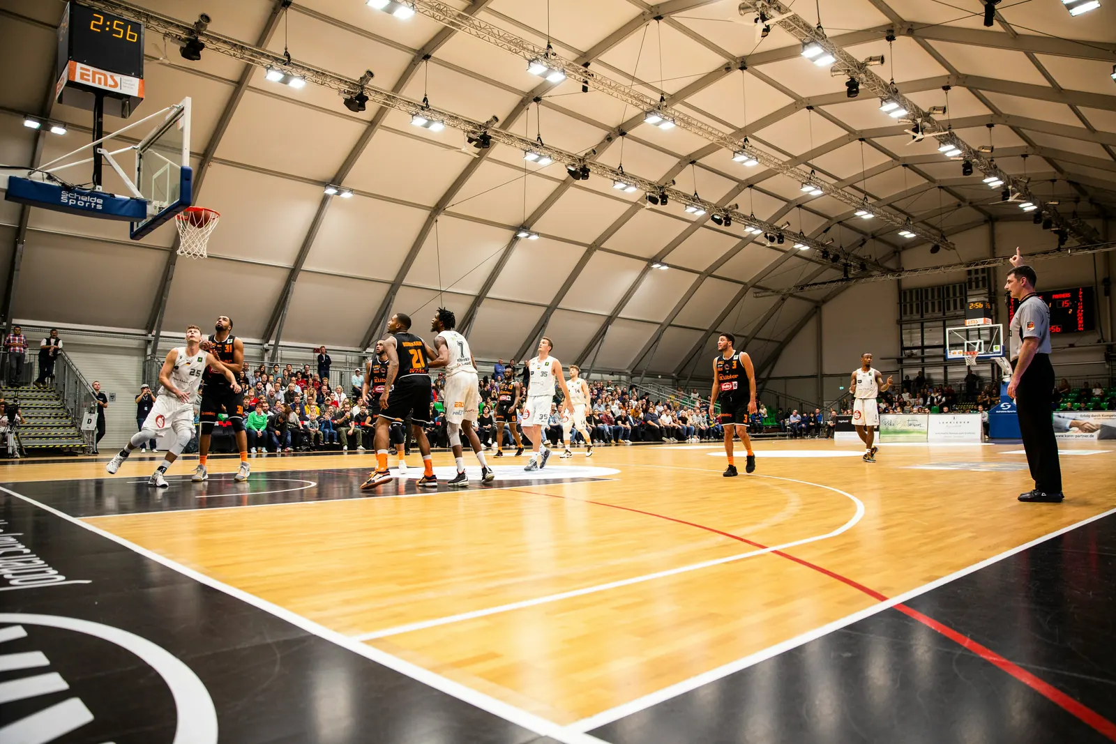 A full basketball game underway on an indoor court, players set either side of the key
