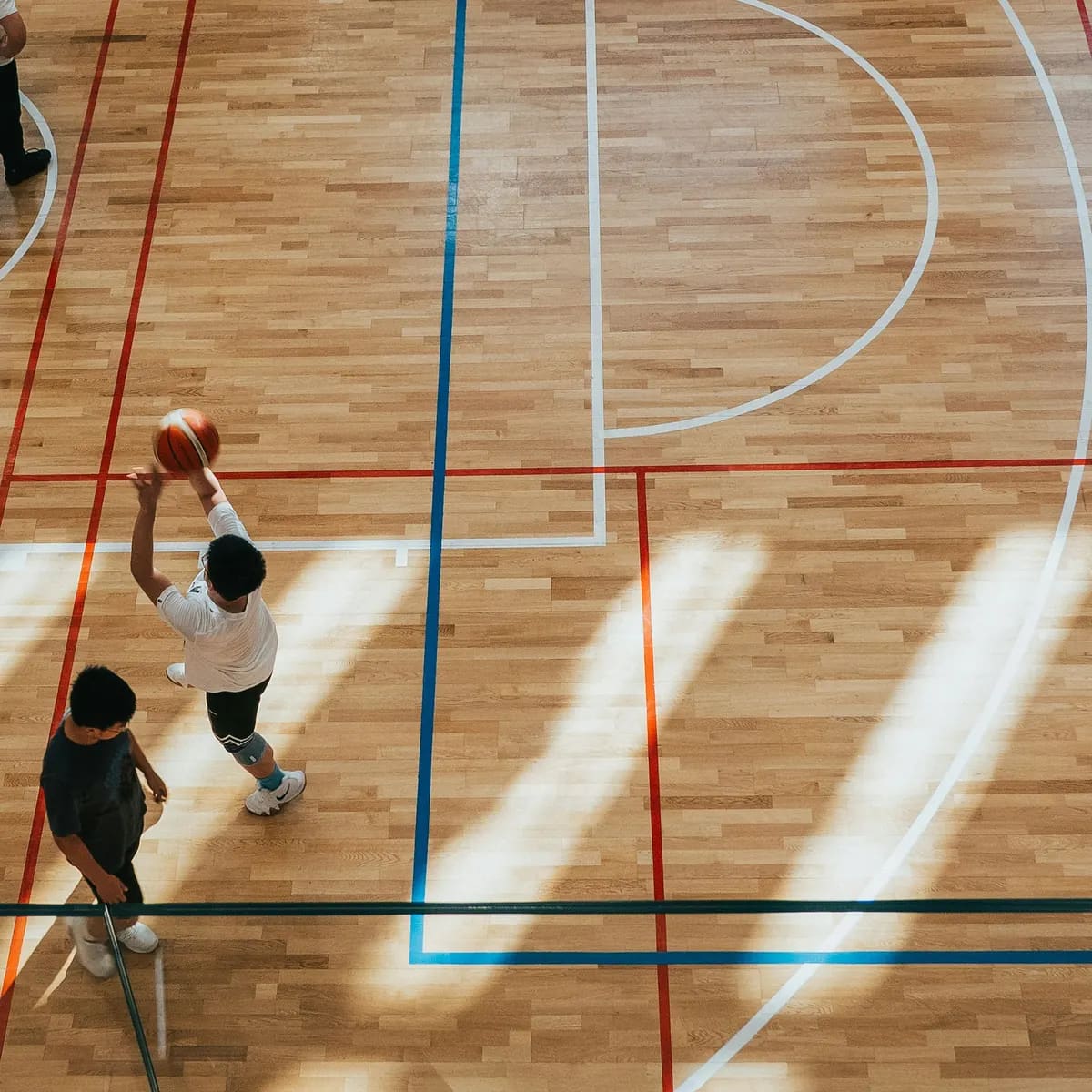 An indoor court from above, a player rising for a shot in the corner of it
