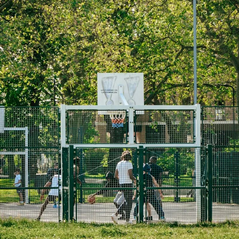 A park basketball court behind a fence, a game going on under the hoop