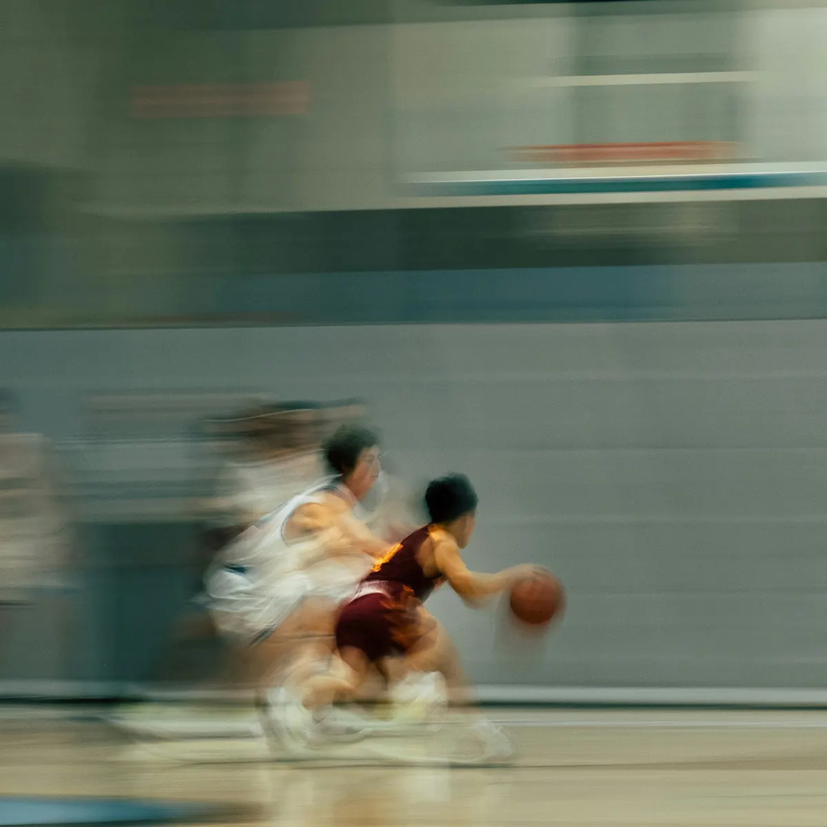 A player driving the ball up an indoor court, the game blurred with the speed of it